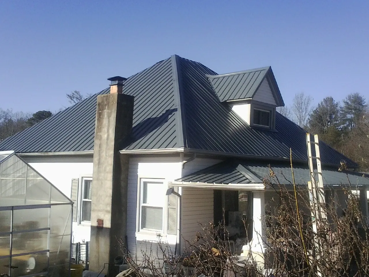 Dark blue standing seam metal roof on a white farmhouse with dormer — Slate & Tile Roof Repair by Roofing Brothers in Lyndonville