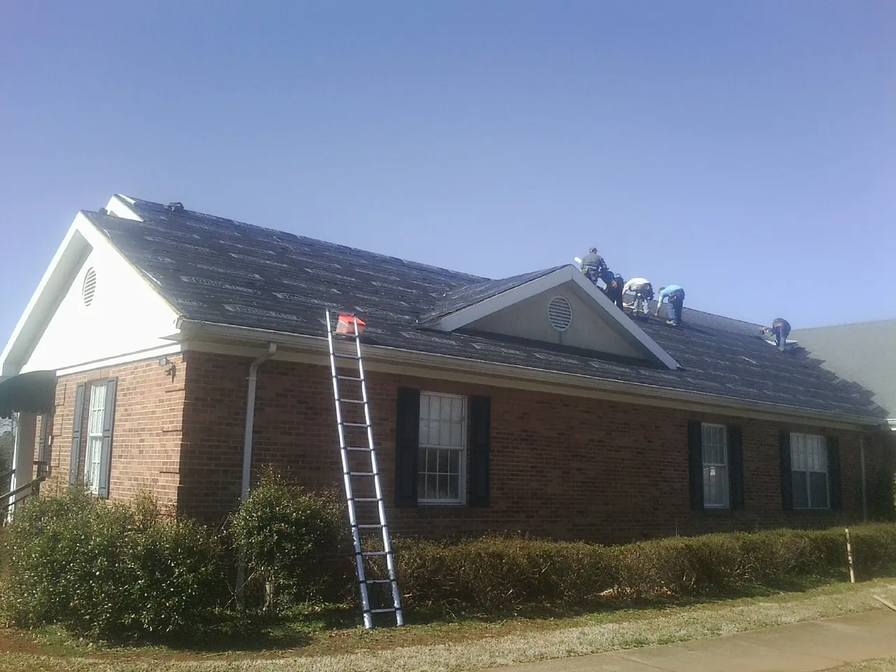 Crew tearing shingles off a brick ranch roof with a ladder set — Emergency Roof Repair work by our crew in Lyndonville