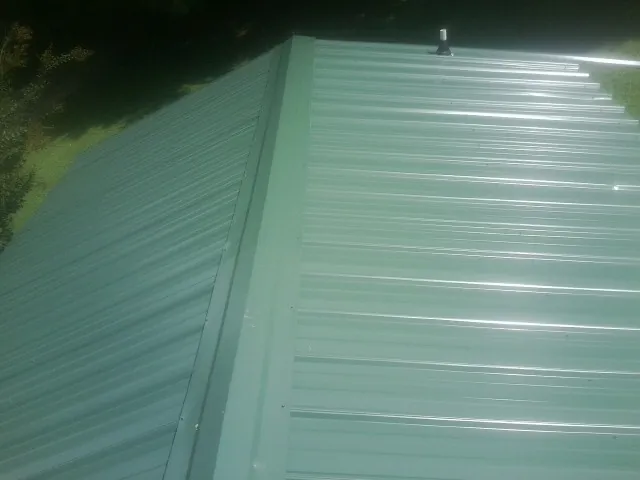 New green metal panels meeting at the ridge of a roof — Flat Roof Repair work by our crew in Lyndonville
